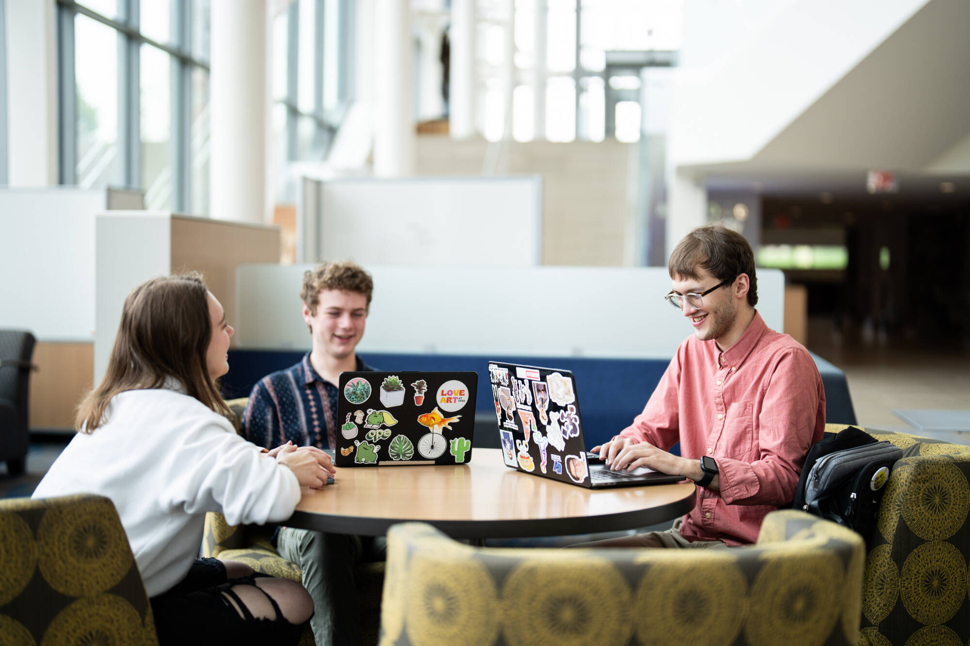 Students sit together at the library laughing and working on laptops.